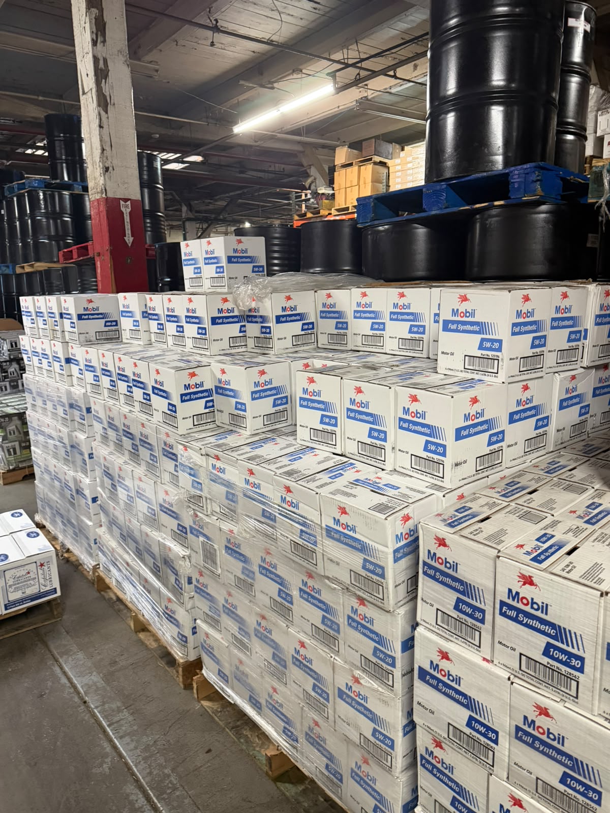 A wall of Mobil Full Synthetic motor oil cases with black drums stacked overhead