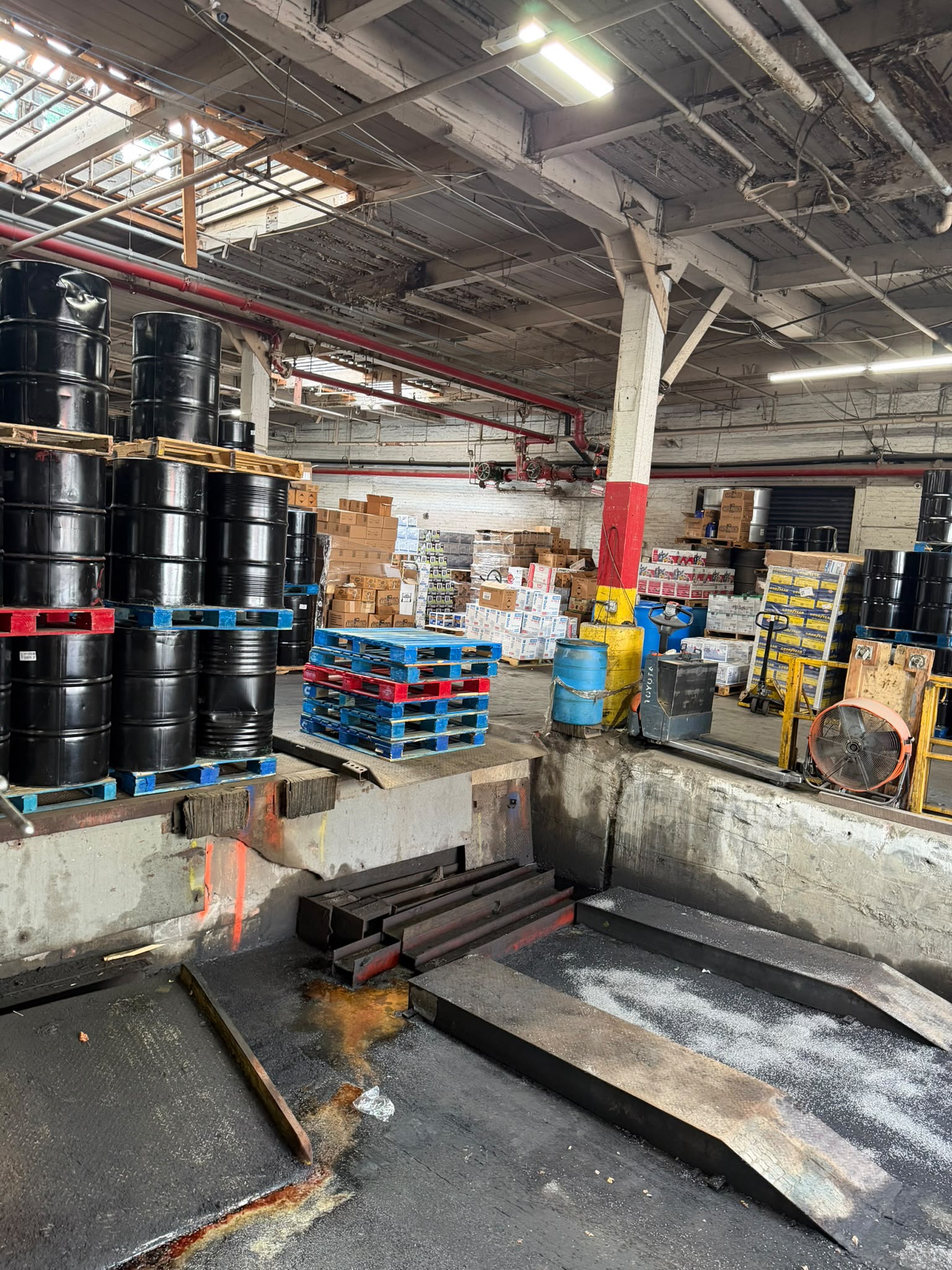 Rows of black oil drums stacked by the loading dock at the Bass Oil warehouse